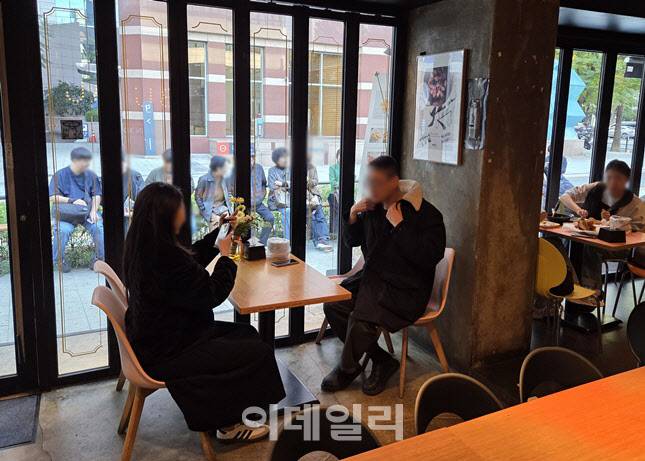 식사 중인 손님 너머, 창밖으로는 줄지어 앉아 입장을 기다리는 인파가 보인다. 총수들의 사진 포스터 앞에서 인증샷을 찍는 한 커플 (사진=한전진 기자)