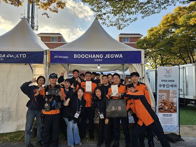 소방관들이 국제미디어센터(IMC) 건너편 천군동 메타세콰이어숲 인근에 마련된 ‘K푸드 스테이션’에서 부창제과 호두과자를 제공 받고 기념촬영을 하고 있다. FG 제공