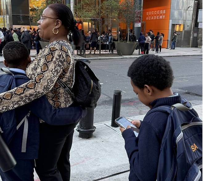 미국 뉴욕 맨해튼 미드타운 웨스트지역 석세스 아카데미에 등교하는 학생들이 휴대전화를 보고 있다. 뉴욕시는 9월부터 모든 공립학교에서 등교부터 하교시까지 휴대전화 사용 금지 정책을 시행하고 있다.