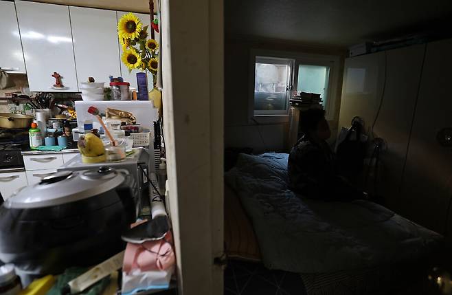 2025년 10월28일 오전 서울 성동구 송정동 반지하 주택에 사는 서윤희씨가 햇빛이 잘 들지 않는 방 침대에 앉아 쉬고 있다. 왼쪽은 주방 겸 거실. 방 전등을 켜지 않아 칠흑처럼 어둡다. 이종근 선임기자 root2@hani.co.kr