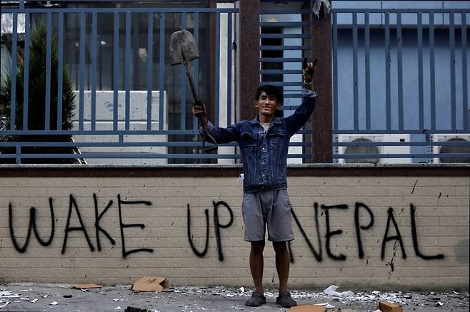 Sabin Tamang, 20, who works in a restaurant and participated in a Gen-Z protest, holds up a shovel while posing for a photograph next to graffiti as he takes part in a cleaning campaign following Monday's deadly anti corruption protests in Kathmandu, Nepal, on Sept. 10. [REUTERS/YONHAP]