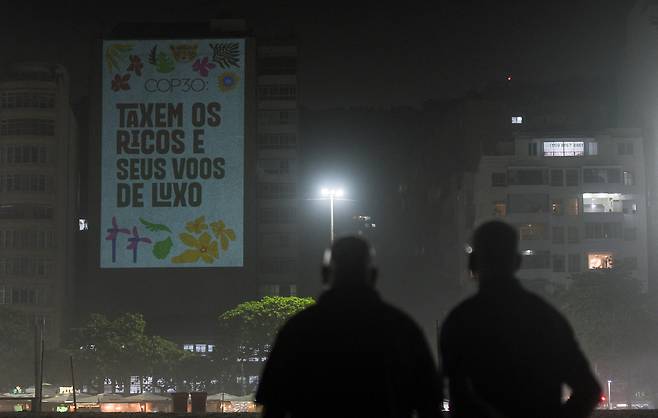 5일 브라질 리우데자네이루에 환경단체 활동가들이 걸어놓은 대형 현수막을 브라질 시민들이 바라보고 있다. 현수막에는 “부자들과 그들의 고급 항공기에 세금을 부과하라”라고 적혀있다. 브라질 벨렝에서는 오는 10일부터 제30차 기후변화협약 당사국총회(COP30)가 열린다. 로이터연합뉴스