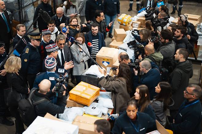 6일 프랑스 루아시 샤를 드골 공항 물류 창고에서 하얀 장갑을 착용한 세관 직원들이 쌓여 있는 ‘쉬인’발(發) 소포를 열어 보는 가운데, 세르주 파팽 중소기업부 장관과 아멜리에 드몽샬랭 공공회계부 장관 등 정부 인사와 취재진이 이들을 둘러싸고 지켜보고 있다. 세관 관계자는 소포 20만개를 열고 위법 물건을 가려내는 데 최소 한 달이 걸릴 것이라고 말했다./ABACAPRESS