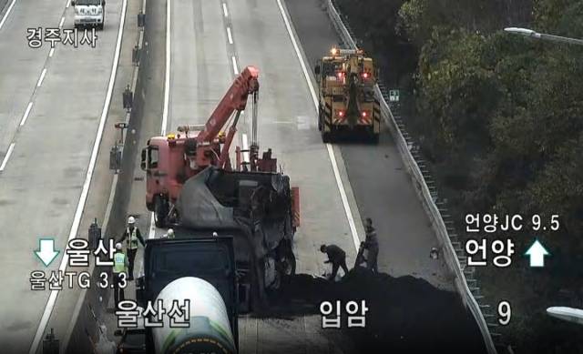 13일 오전 울산고속도로 언양 방면 범서IC 인근 사고 현장에서 관계자들이 전도된 화물트럭을 견인하고 도로에 쏟아진 석탄을 수습하고 있다. 이날 사고로 일대 2개 차로가 한때 통제되며 극심한 정체를 빚었다. 고속도로 교통정보 CCTV 캡처. 연합뉴스