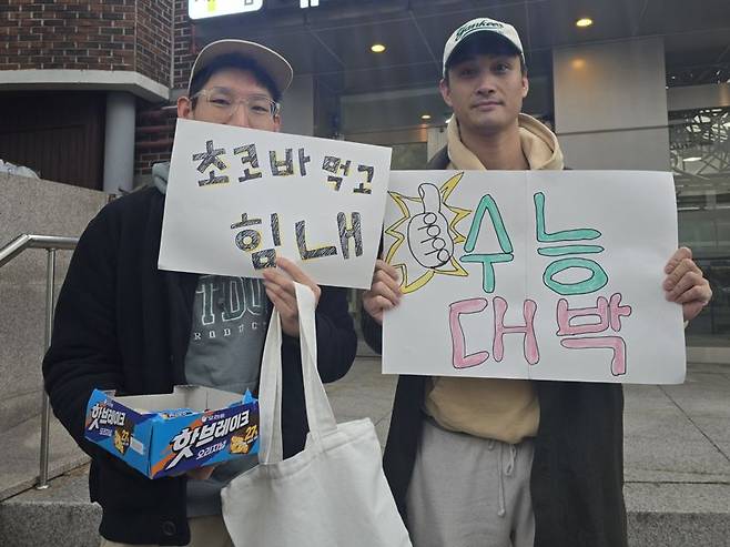 2026학년도 대학수학능력시험(수능) 당일인 13일 오전 서울 종로구 경복고등학교 앞에서 황모씨(35, 왼쪽)가 지인 왈리씨(40)와 수험생들을 응원하고 있다. 사진=서지윤 기자