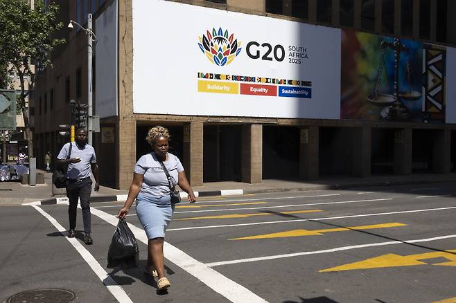 13일(현지시간) 남아프리카공화국 요하네스버그 도심에서 보행자들이 G20 정상회의 광고판 앞을 지나가고 있다. [EPA}