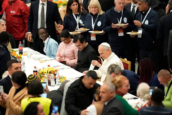 교황 레오 14세(식탁 왼쪽에서 네 번째)가 16일(현지 시간) 바티칸의 바오로6세홀에서 ‘가난한 이들의 희년’을 기념해 노숙인, 장애인, 난민 등 취약계층 1300여 명을 초청한 점심 식사 행사에서 식사 준비를 하고 있다. 바티칸시티=AP 뉴시스