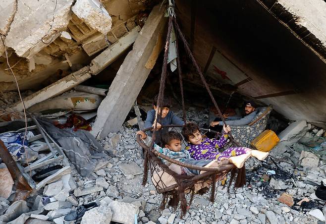 19일(현지시각) 가자지구 북부에서 팔레스타인 어린이들이 파괴된 건물 잔해에 설치한 그네를 타고 있다. 로이터 연합뉴스