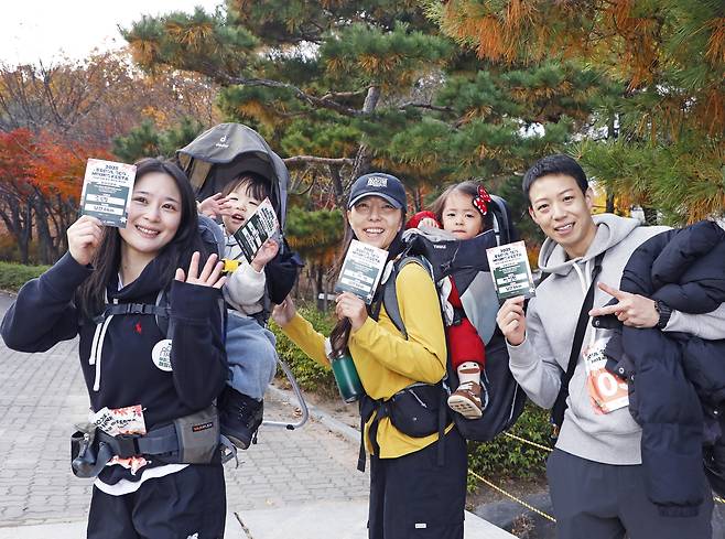 Participants of the 2025 Seoul Eco Hiking Festa pose for a photo with their completion certificates, carrying their children after hiking along a trail on Mount Namsan in Jung District, central Seoul, during the event’s family-themed hike on Nov. 22. [PARK SANG-MOON]