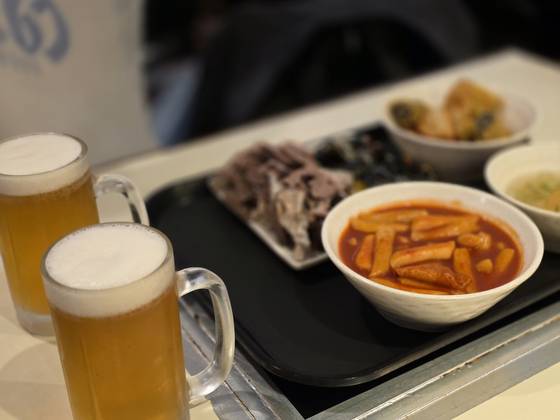 Tteokbokki (spicy rice cakes) served with fried side dishes and sundae (Korean blood sausage) next to draft beers [JIN EUN-SOO]