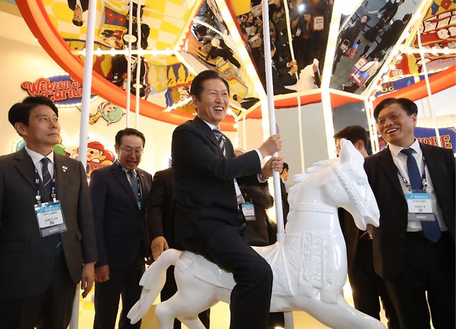 정청래 더불어민주당 당대표가 14일 부산 해운대구 벡스코에서 열린 ‘지스타 2025’를 찾아 웹젠이 마련한 포토존에서 회전목마를 타고 있다. [뉴스1]