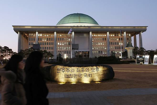 On Dec. 2, the day before the first anniversary of the emergency martial-law crisis, people walk past a symbolic stone engraved with “National Assembly of the Republic of Korea, the Last Bastion of Democracy” at the National Assembly in Seoul’s Yeouido district. [YONHAP]