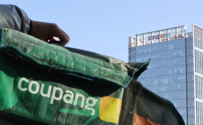 The reporter holds up a Coupang Fresh Bag in front of the company headquarters in Songpa District, southern Seoul, on Dec. 1. [YONHAP]