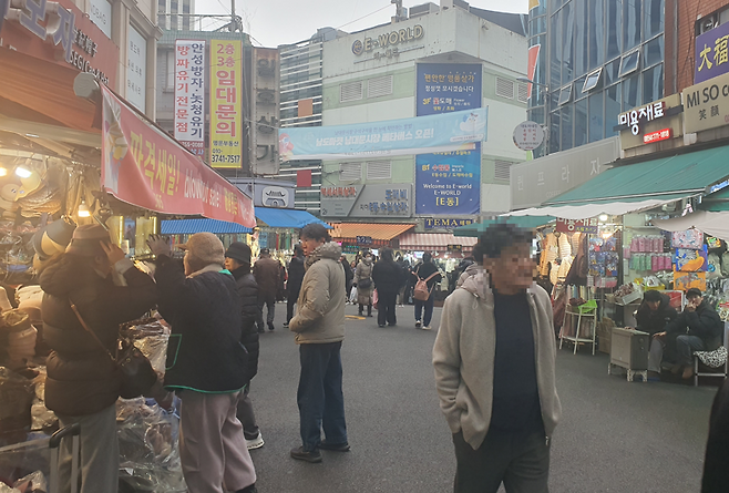 지난 6일 오후 서울 중구 남대문시장에서 손님들이 모자를 시착하고 있다. 한켠에는 시장 상인들이 난로 앞에서 몸을 녹이는 모습. 사진=최승한 기자