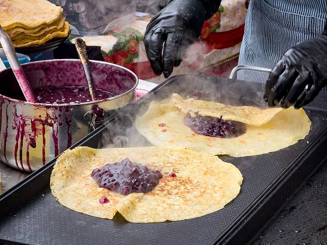 A woman folds warm pancakes filled with blueberry compote at the Bulgarian booth of the European Market in Seongbuk District, central Seoul, on Dec. 6. [MICHAEL LEE]