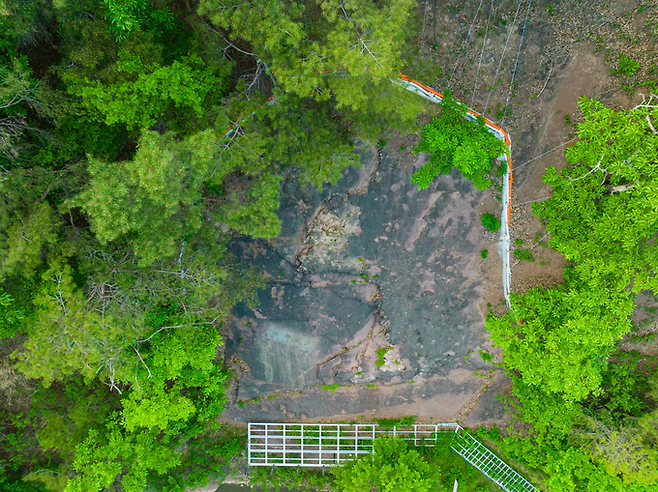▲ 경북 의성군 금성면 만천리 아기공룡 발자국 화석지에서 드론 촬영 화면이 울창한 숲 사이로 드러난 암반 위 1억 년 전 새끼 공룡 보행렬을 위에서 포착해, 화석 보호 울타리와 주변 식생 분포까지 한눈에 담아냈다. 의성군