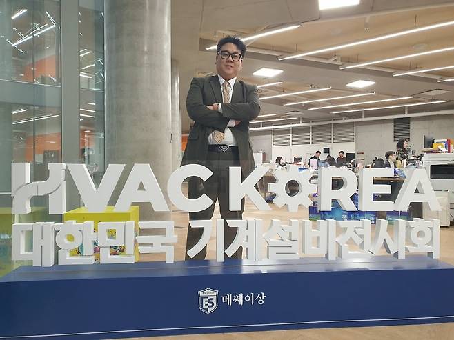 박용섭 매니저가 대한민국 기계설비전시회 로고 앞에서 포즈를 취하고 있다. 윤현주 기자