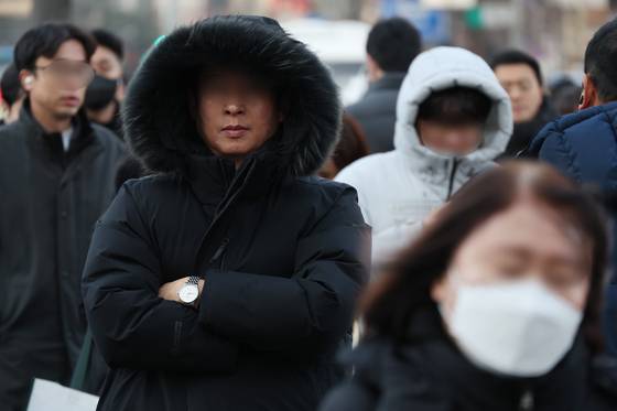 People clad in thick coats, mufflers and gloves walk on a street near Gwanghwamun Square in Jongno District, central Seoul on Dec. 12. [YONHAP]