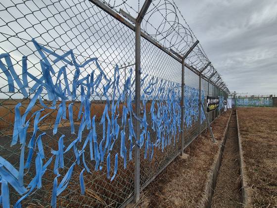 12·29 제주항공 여객기 참사 1주기를 사흘 앞둔 지난 26일 전남 무안국제공항 사고 현장 인근 철조망에서 희생자들을 추모하는 하늘색 리본이 나부끼고 있다. 황희규 기자
