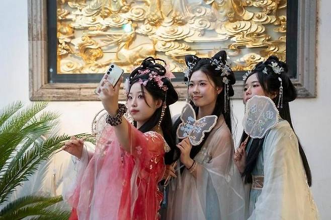 Tourists from Korea wearing Hanfu outfits take a selfie at Yuyuan Garden Mall in Shanghai on July 21. [XINHUA/ZHANG YUE]