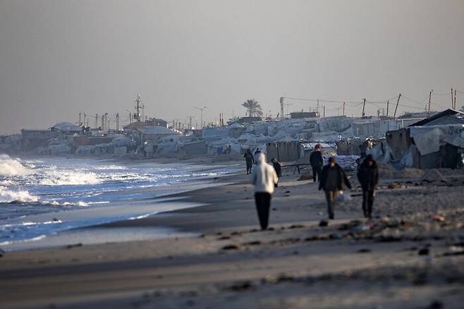 1일 가자지구 남부 칸 유니스시 해안에서 피란민 팔레스타인 주민들이 머무는 천막들 앞 해변을 주민들이 걷고 있는 모습. EPA 연합뉴스