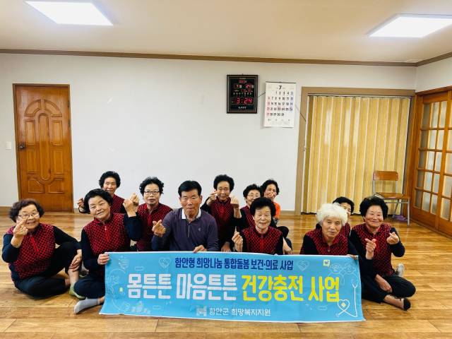 함안 지역의 한 경로당에서 어르신들이 희망나눔 통합 돌봄 보건의료 사업 현수막을 들고 손하트를 하고 있다./함안군/