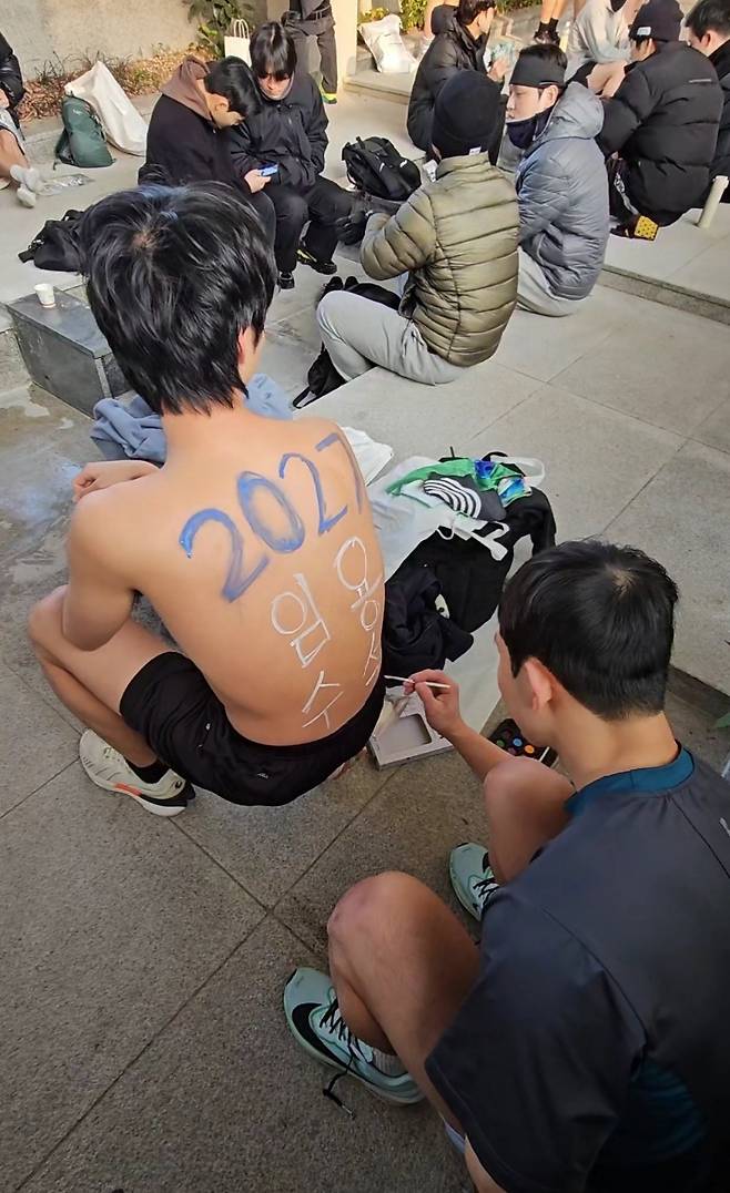 Song In-hyuk’s friend paints words on his back that read “Imyong Suseok,” meaning the top score in the public school teacher recruitment exam. (Choi Jae-hee/The Korea Herald)