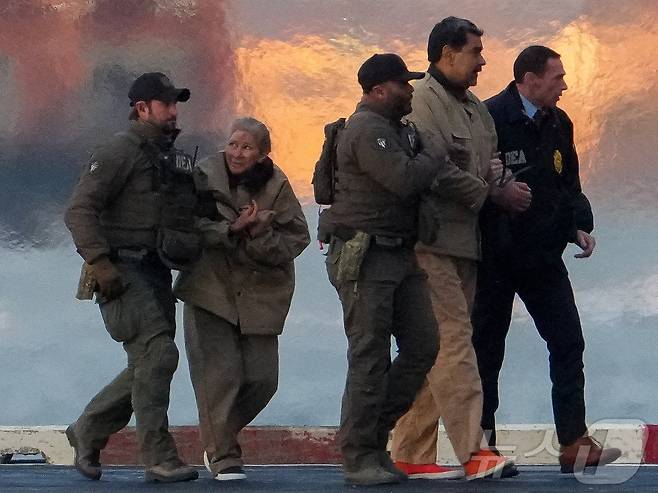 미국 마약단속국(DEA) 요원들이 체포된 니콜라스 마두로 베네수엘라 대통령과 부인 실리아 플로레스를 헬리콥터에서 내리게 하고 있다. 2026.01.05. ⓒ 로이터=뉴스1 ⓒ News1 이정환 기자