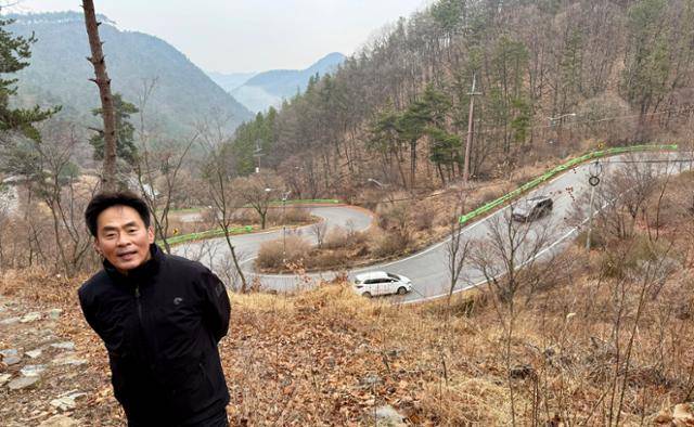 숲길 탐방에 동행한 최원석 (사)속리산둘레길 사무국장이 말티재 숲길을 따라 오르던 중 12굽이 도로를 배경으로 포즈를 취했다. 숲길은 일부 지역에서 차도를 가로지르지만, 대부분 차도와 분리된 채 이어진다.