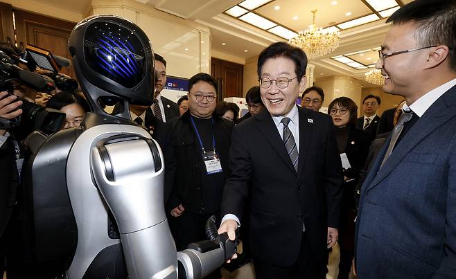 President Lee Jae Myung, center, shakes hands with a humanoid robot made by a Chinese company during the Korea-China Venture Startup Summit in Shanghai on Jan. 7. [JOINT PRESS CORPS]