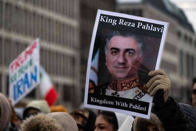 지난 12일(현지시간) 독일 베를린 브란덴부르크 문 앞에서 열린 반이란 정부 시위에서 한 시위자가 이란 왕조의 마지막 왕세자 레자 팔레비의 초상화가 그려진 플래카드를 들고 있다. AFP연합뉴스