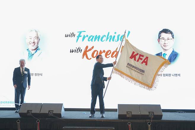▲ 나명석 한국프랜차이즈산업협회장이 지난 19일 서울 여의도 콘래드호텔에서 정현식 전임 회장으로부터 전달받은 협회장기를 힘차게 흔들어 보이고 있다. /사진제공=한국프랜차이즈산업협회