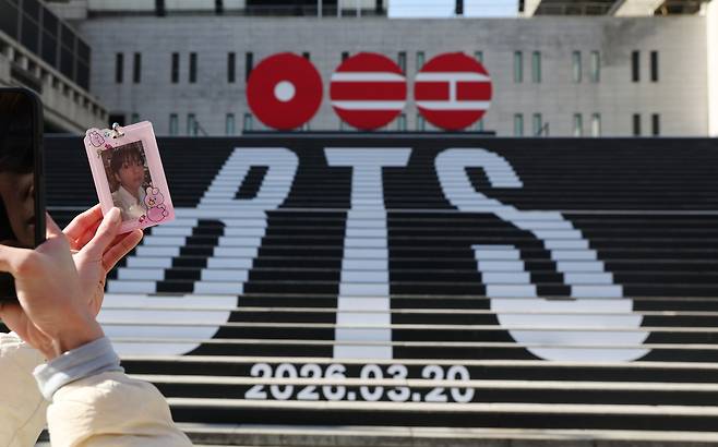 A fan takes a photo with a photo card of BTS' Jungkook in front of the stairs at the Sejong Center for the Performing Arts, which features a sculptural installation of BTS’ new album logo, in central Seoul on Thursday. (Yonhap)