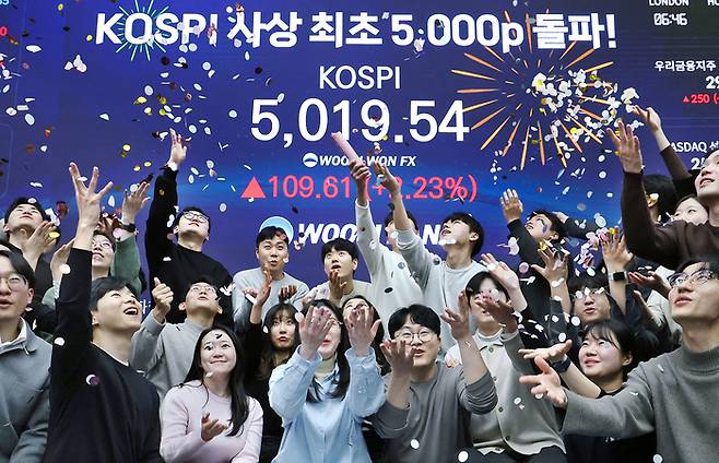 (서울=뉴스1) 오대일 기자 = 한국 증시가 사상 처음으로 ‘코스피 5000’ 쾌거를 달성한 22일 서울 중구 우리은행 본점 딜링룸에서 직원들이 장중 최고가가 찍힌 전광판을 배경으로 코스피 5000 돌파를 축하하고 있다.  이날 코스피는 이재명 대통령이 ‘코스피 5000’ 공약을 내걸고 임기를 시작한 지 7개월 만에 장중 꿈의 5000을 돌파하며 한국 자본시장의 역사를 새로 썼다. [뉴스1]