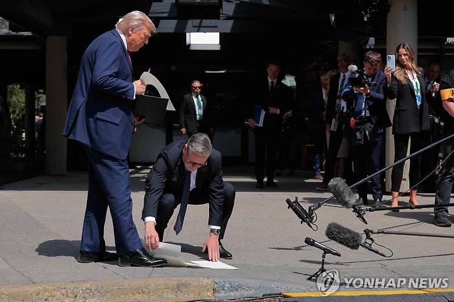 2025년 6월 16일 트럼프 대통령이 떨어뜨린 미영 무역협정 서류를 줍는 스타머 총리 [AFP/게티이미지 연합뉴스 자료사진. 재판매 및 DB 금지]