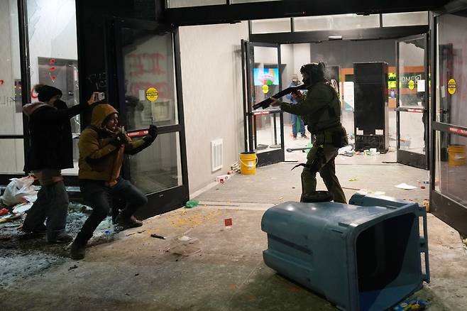 미국 미네소타주 미니애폴리스에서 25일(현지시간) 한 연방요원이 호텔 밖에서 이민단속 반대 시위를 벌이는 시민을 향해 총을 겨누고 있다. (미니애폴리스(미국)/AP연합뉴스)