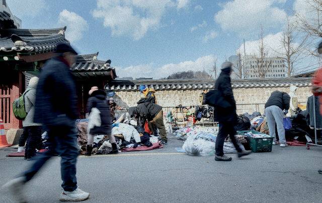 바닥에 깔린 천 위에 옷이 수북이 쌓여 있고, 사람들은 몸을 낮춘 채 저마다의 보물을 찾아 손을 움직인다.