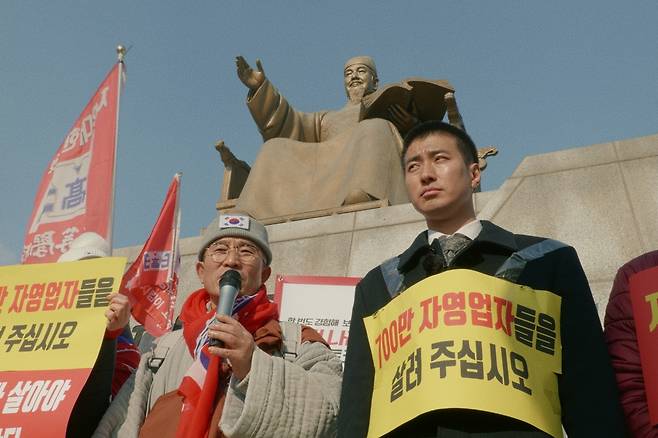 김현진(오른쪽)이 서울 종로구 광화문광장 세종대왕동상 앞에서 ‘700만 자영업자들을 살려주십시오’라고 쓰인 종이를 몸에 붙인 채 시위에 참여하고 있다. 익스포스 필름 제공