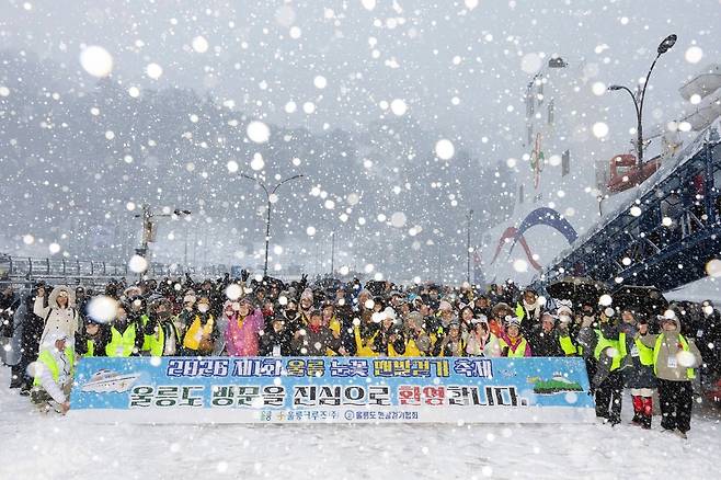 제1회 울릉 눈꽃 맨발 걷기 축제에 참여하기 위해 울릉 크루즈를 타고 입도한 경북 동호인들이 눈이 펑펑 내리는 사동항에서 단체 기념 사진을 찍고 있다. /울릉크루즈 제공