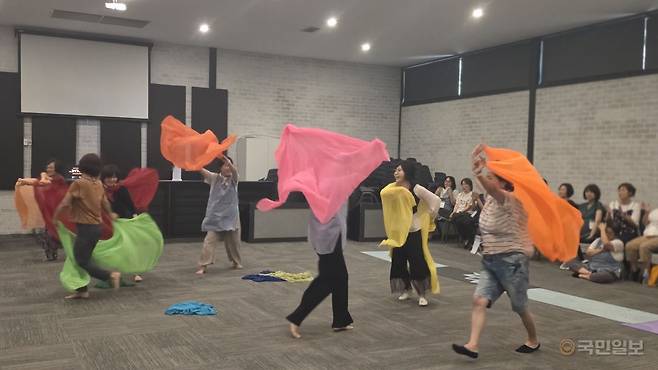 참석자들이 신체심리치료 프로그램의 하나로 서로 어깨동무하며 노래를 부르고 있다. 아래 사진은 참석자들이 둘씩 서로 짝을 지어 서로를 안아주며 위로하는 모습과 마지막날 진행된 스킷드라마 시간에 형형색색의 천을 들고 나비를 표현하고 있는 참가자들 모습이다.