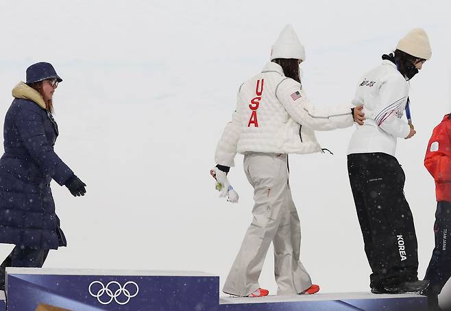 12일(현지시간) 이탈리아 리비뇨 스노파크에서 열린 2026 밀라노-코르티나담페초 동계올림픽 스노보드 여자 하프파이프 결승에서 금메달을 따낸 최가온이 메달 세리머니를 마치고 클로이 김의 부축을 받으며 시상대를 내려가고 있다.
