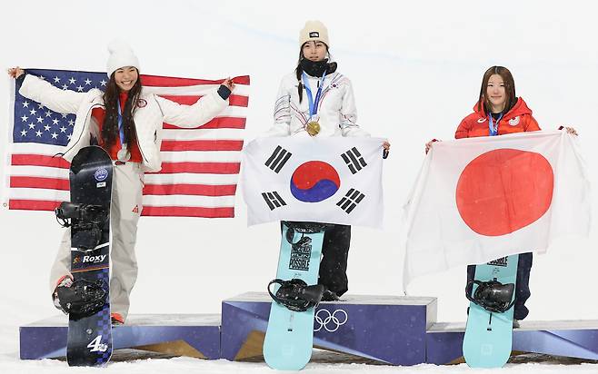 13일 이탈리아 리비뇨 스노파크에서 열린 2026 밀라노·코르티나담페초 동계 올림픽 스키 스노보드 여자 하프파이프 결선에서 90.25점을 획득해 금메달을 획득한 한국 최가온이 시상대에 올라 태극기를 펼치고 있다. 왼쪽은 은메달을 딴 미국의 레전드 클로이 김. [연합]
