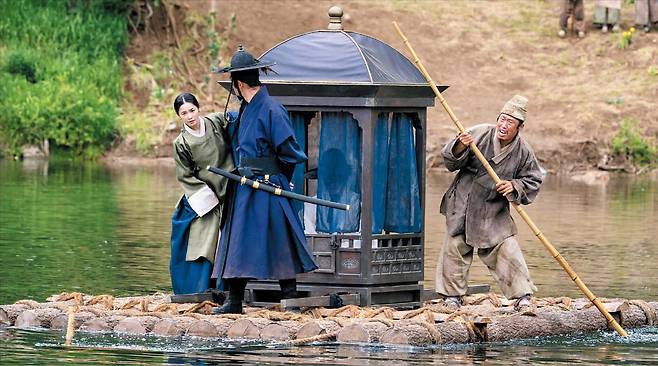 영화 ‘왕과 사는 남자’ 중 단종(박지훈·가마 속 인물)이 탄 뗏목의 노를 엄흥도(유해진·오른쪽)가 저으며 유배지인 청령포로 가고 있다. 영화와는 달리 단종은 실제로는 유배지에서 빠져나올 수 없었다./쇼박스