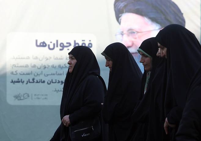 17일 이란 테헤란의 모살라 모스크에서 열린 반정부 시위 희생자 추모식에 참석하기 위해 도착한 이란 최고 지도자 아야톨라 알리 하메네이의 포스터 옆을 이란 여성들이 걸어가고 있다. EPA연합뉴스