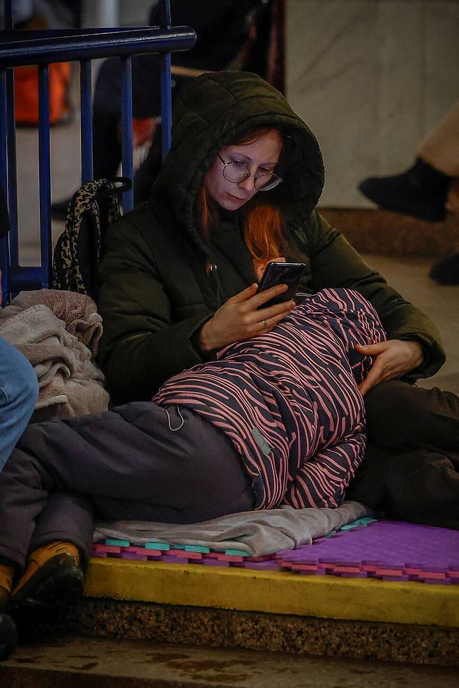 22일(현지시각) 우크라이나 키이우에서 러시아의 미사일, 드론 공격을 피해 지하철역 안으로 대피한 한 여성이 아이를 안고 휴대폰을 보고 있다. 로이터 연합뉴스