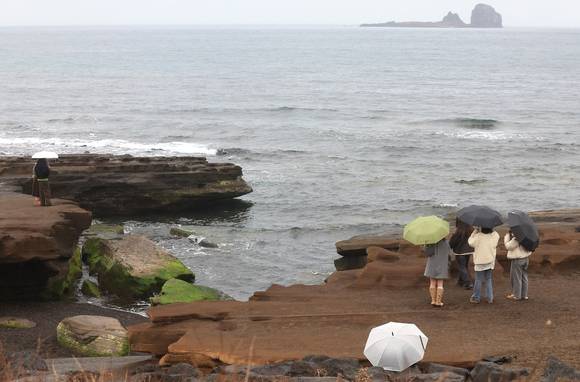 겨울비가 내리는 속 제주 서귀포시 안덕면 사계리 해안을 찾은 관광객이 우산을 들고 바닷가 정취를 즐기고 있다. [사진=연합뉴스]