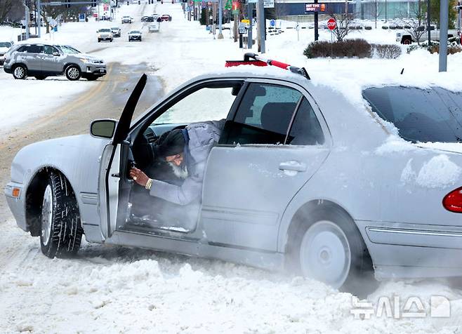 [세인트앤=AP/뉴시스]  미 미주리주 세인트앤의 한 주민이 지난 1월 6일 눈 때문에 도로에서 바퀴가 헛도는 차량을 빼내려 하고 있다.미 중·동부에 내린 폭설로  정전과 교통마비 등 피해가 잇따르고 2월 22일 부터 뉴욕 등 일부지역 통행금지도 실시된다. 2026.02.23.