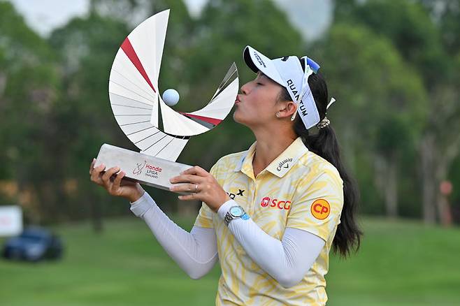 [파타야=AP/뉴시스] 지노 티띠꾼(태국)이 22일(현지 시간) 태국 파타야 시암 컨트리클럽에서 열린 미국여자프로골프(LPGA) 투어 혼다 타일랜드 정상에 올라 트로피를 들고 입 맞추고 있다. 티띠꾼은 최종 합계 24언더파 264타로 우승을 차지했다. 2026.02.23.