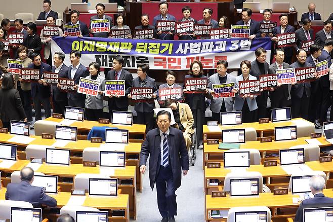 27일 국회에서 열린 2월 임시국회 8차 본회의에서 전날 상정된 헌법재판소법 일부개정법률안(재판소원제)에 대한 무제한 토론(필리버스터) 종결을 위한 투표가 시작되자 국민의힘 의원들이 손팻말과 피켓을 들고 시위를 펼치는 가운데 민주당 정청래 대표가 우원식 국회의장에게 항의한 뒤 국민의힘 의원들을 지나쳐 이동하고 있다./연합뉴스