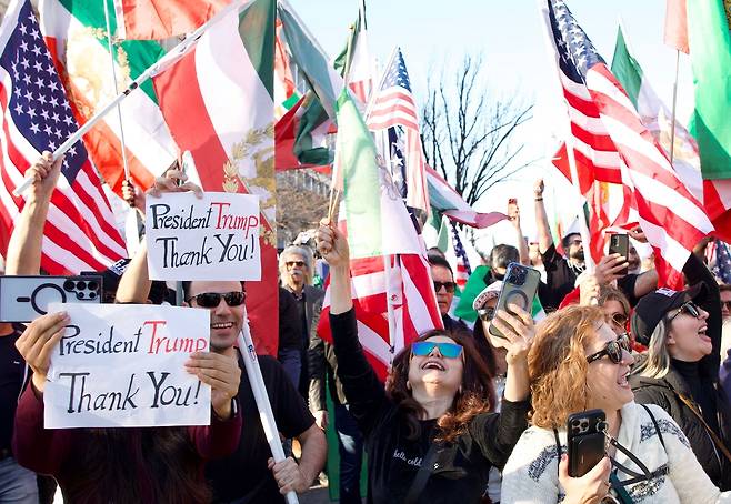 미국 워싱턴 D.C.에서 28일(현지시간) 미국과 이스라엘의 대이란 공격을 지지하는 집회가 열린 가운데, 참가자들이 이란 국기와 미국 국기를 흔들고 “Thank You President Trump(고맙습니다, 트럼프 대통령)”라는 문구가 적힌 팻말을 들며 환호하고 있다. [AFP]
